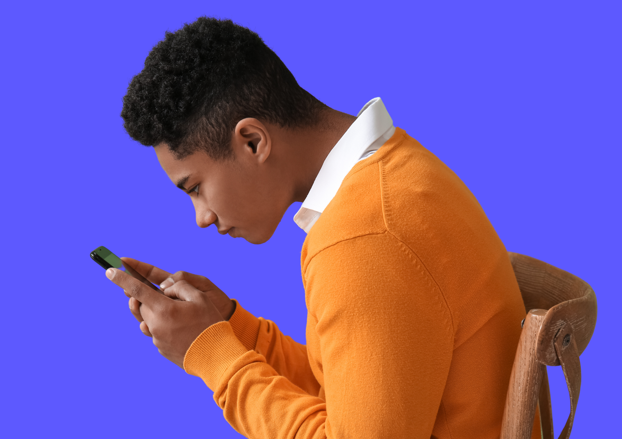 Junge in orangem Pullover starrt mit nach vorne gebeugtem Nacken auf Handy.