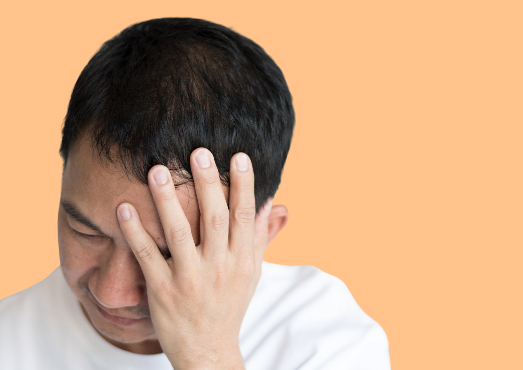 Man holds on to his aching head. Orange background.