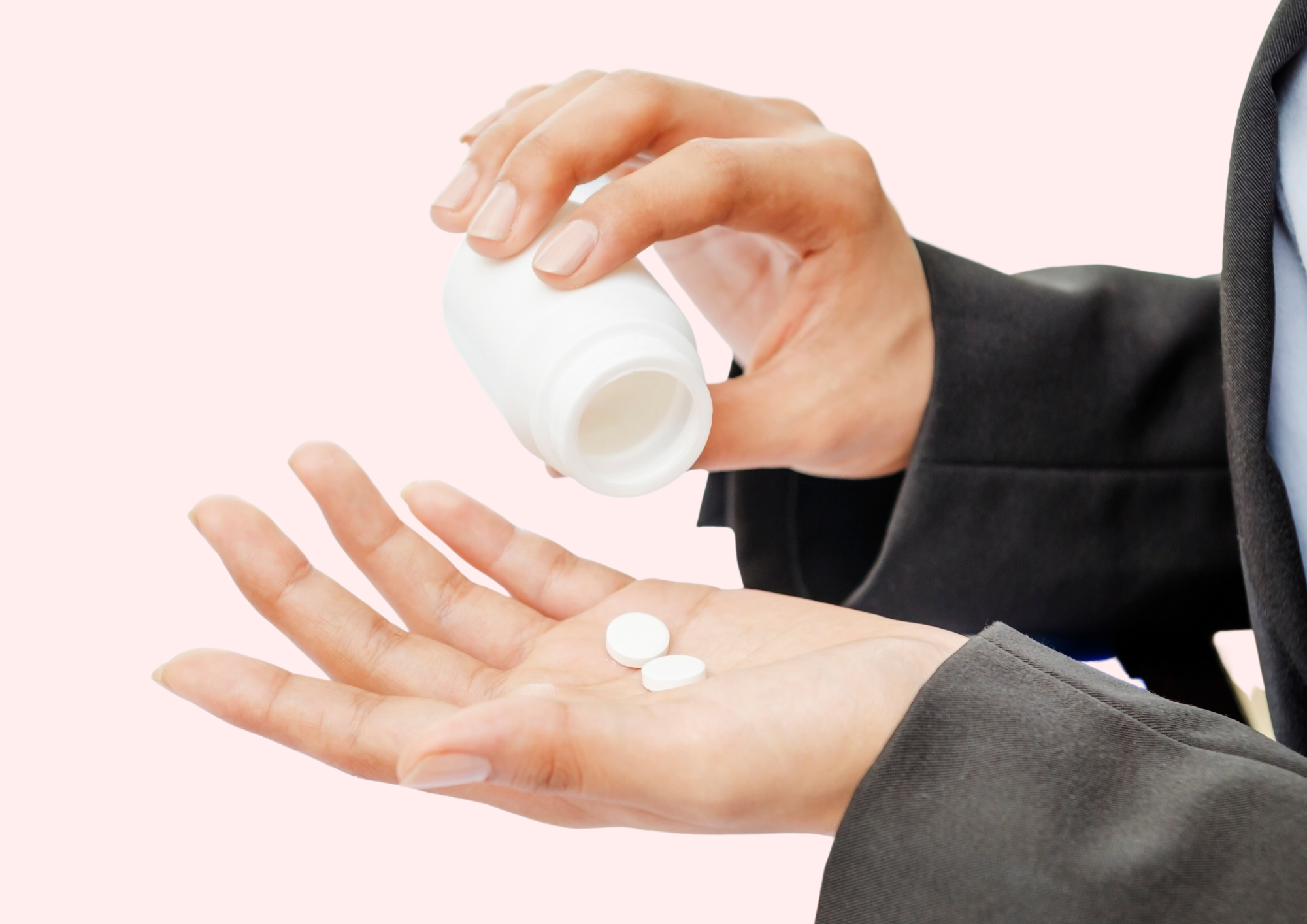 Woman is pouring pills onto her hand. Pink background.